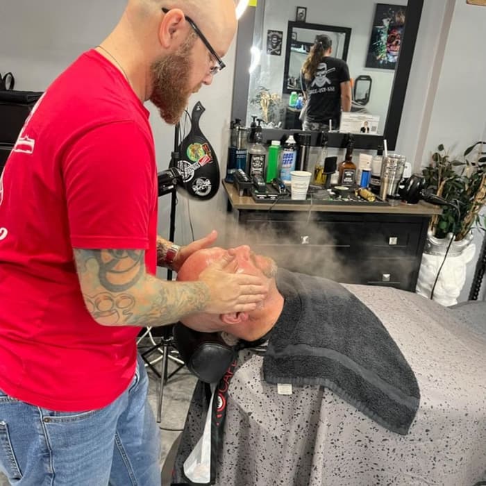 Barber giving a reclined client a steam and hot towel treatment
